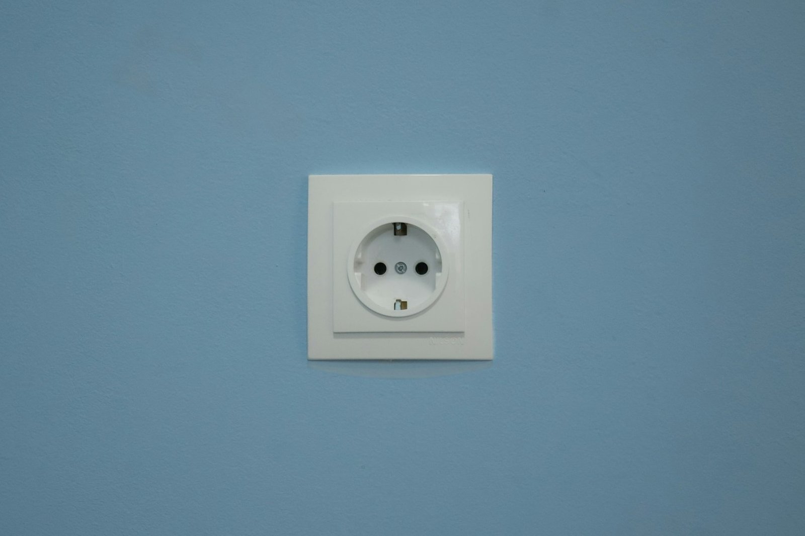 Steckdose mit leicht gelöstem weißen Rahmen an einer Wand